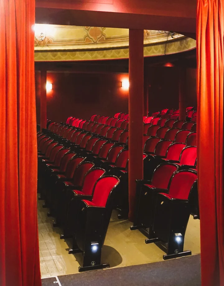Blick durch einen roten Vorhang in einen Theatersaal
